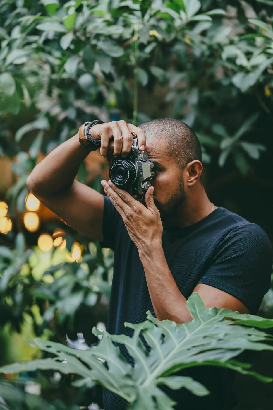 Marcos Prado fotografando com uma câmera Fujifilm entre folhagens