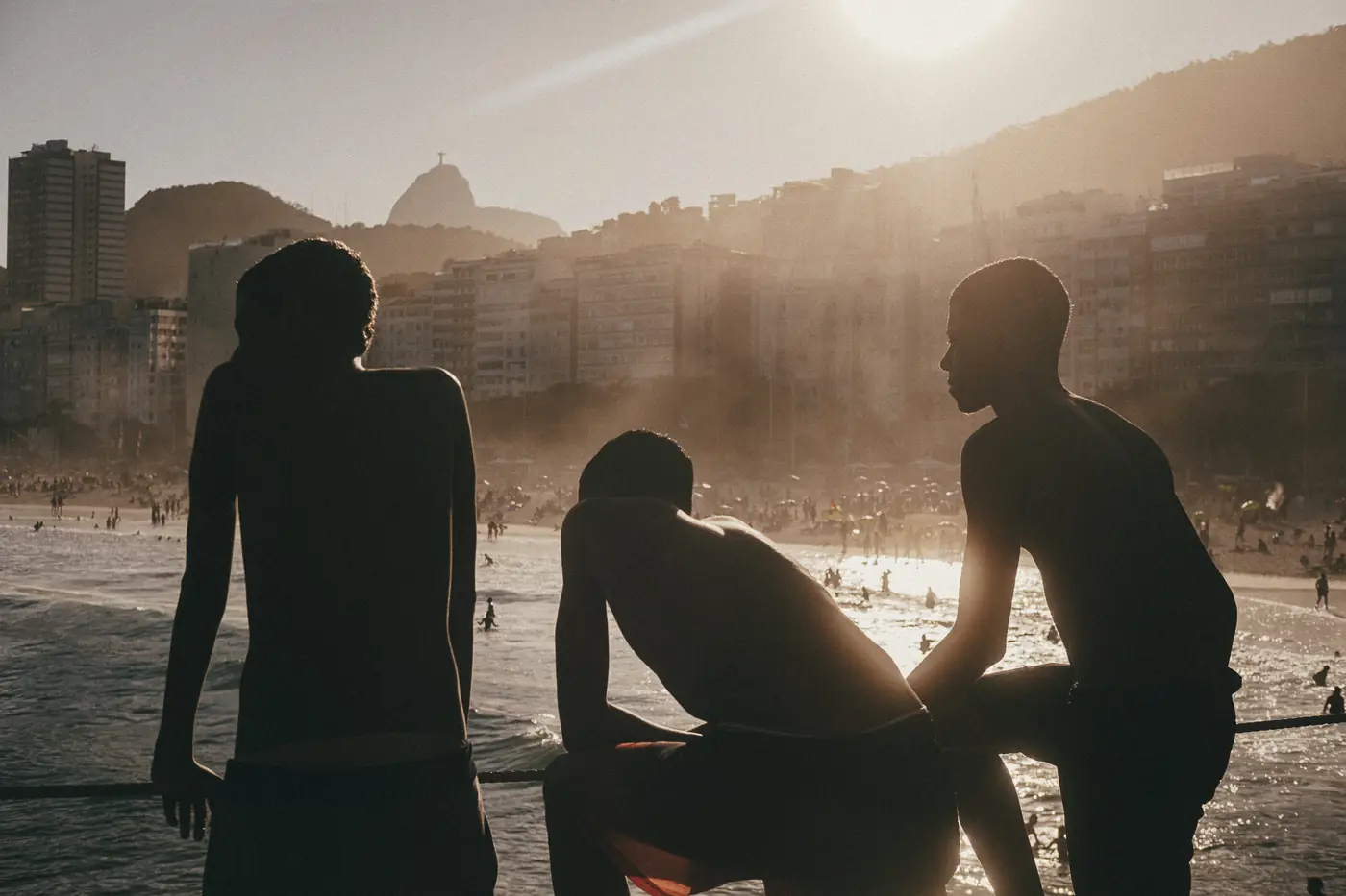 Três jovens em silhueta observando a praia ao entardecer