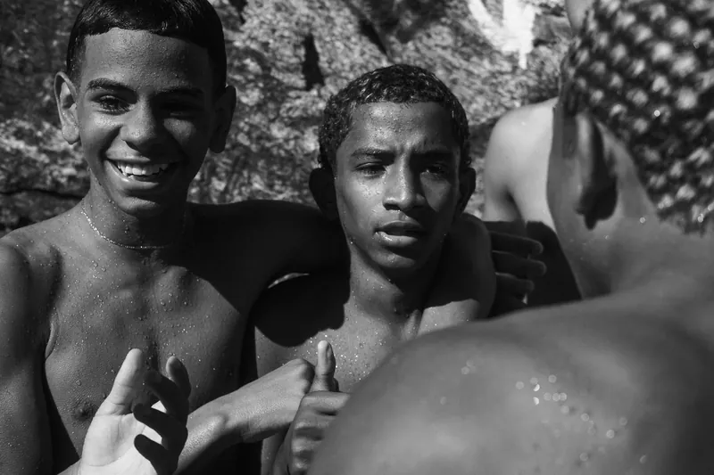 Garotos sorrindo, molhados, depois do banho de mar nas pedras do Rio de Janeiro, em preto e branco.