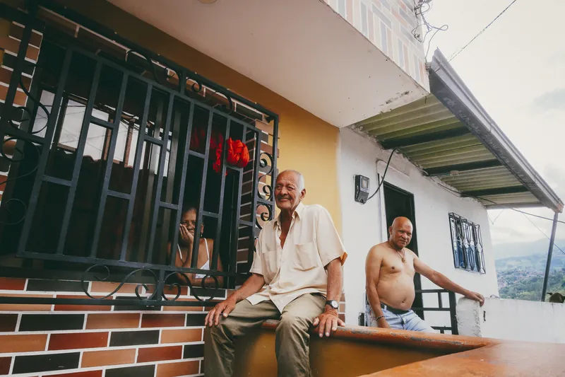 Dois senhores e uma mulher na janela conversam na varanda de uma casa em um bairro alto.