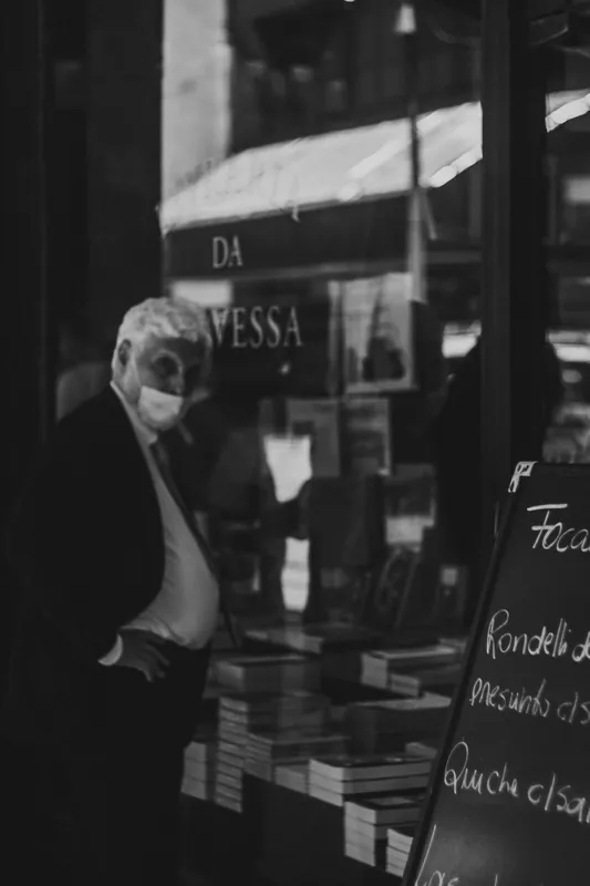 Senhor observa livros na porta de uma livraria, em preto e branco.