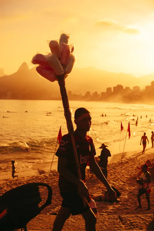 Vendedor de algodão doce caminhando na areia contra a luz dourada do fim de tarde.