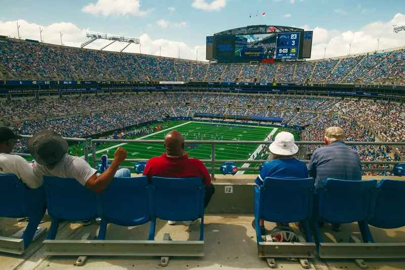 Torcedores assistindo a um jogo da arquibancada alta de um estádio.