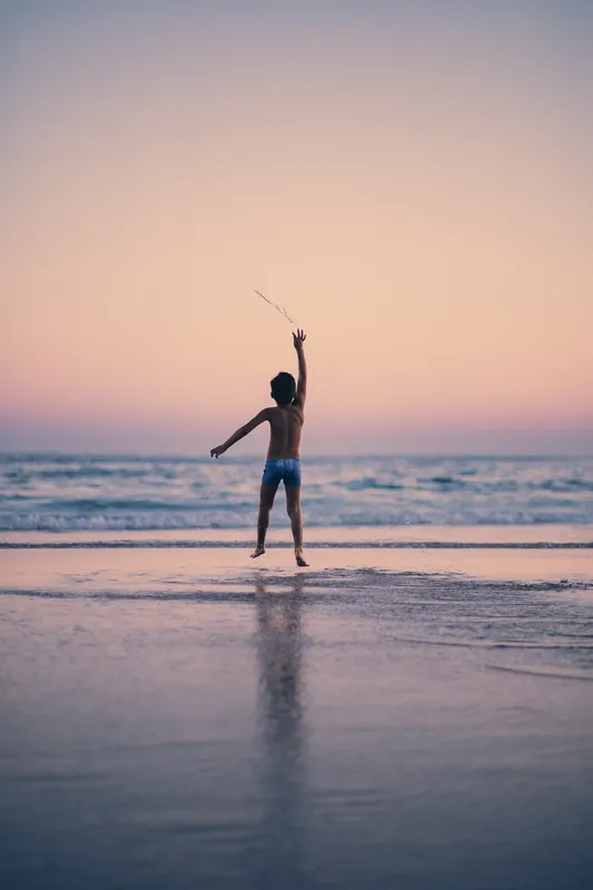 Cópia impressa de um menino saltando na beira do mar no fim de tarde.